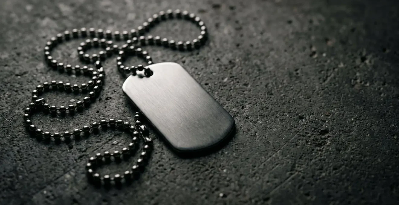 Plaque militaire dog tag en acier posée sur surface minérale avec chaîne à boules dans une ambiance urbaine sophistiquée
