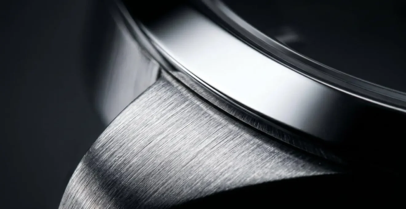 Gros plan sur un boitier de montre montrant les contrastes entre surfaces polies miroir et brossees sous un eclairage dramatique