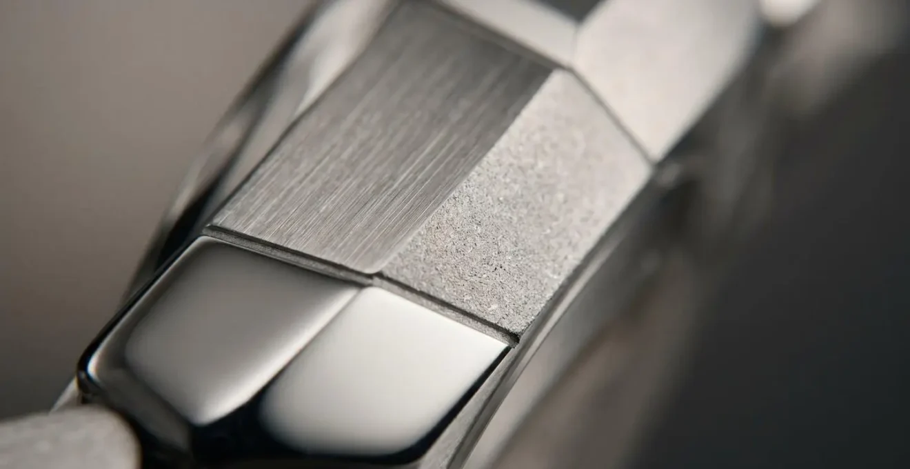 Gros plan sur un boîtier de montre révélant trois finitions contrastées : poli miroir brillant, brossé mat et sablé texturé