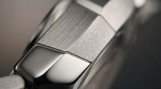 Gros plan sur un boîtier de montre révélant trois finitions contrastées : poli miroir brillant, brossé mat et sablé texturé