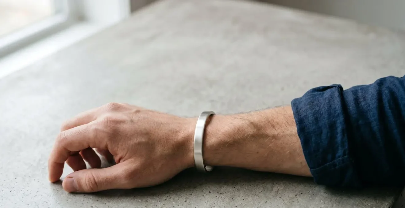 Gros plan sur un poignet masculin portant un jonc rigide ovale en argent mat, photographié dans une lumière naturelle douce mettant en valeur le confort anatomique du bracelet