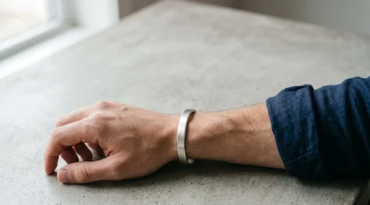 Gros plan sur un poignet masculin portant un jonc rigide ovale en argent mat, photographié dans une lumière naturelle douce mettant en valeur le confort anatomique du bracelet